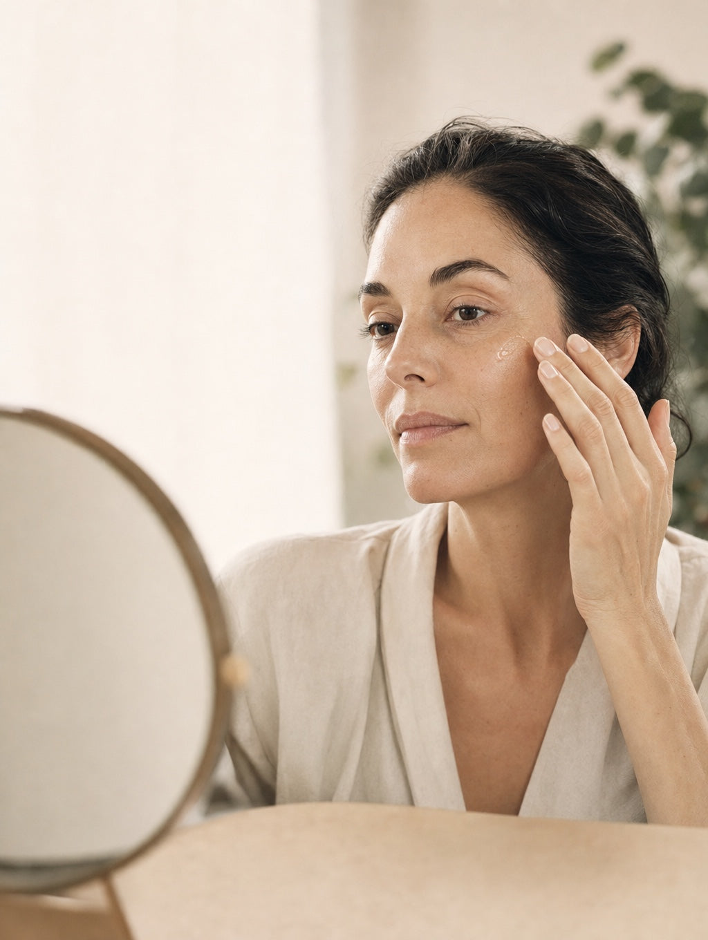 Woman applying Veris serum, looking in a mirror